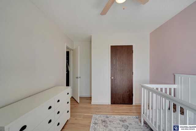 bedroom featuring a crib, ceiling fan, and light hardwood / wood-style flooring