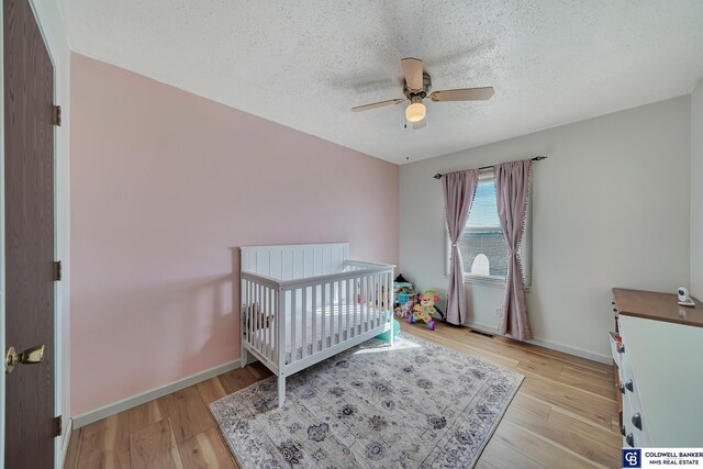 bedroom featuring a crib, a textured ceiling, light wood-type flooring, and ceiling fan