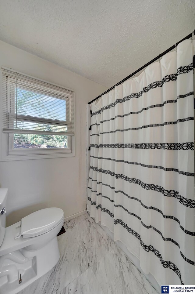 bathroom with a textured ceiling, curtained shower, and toilet