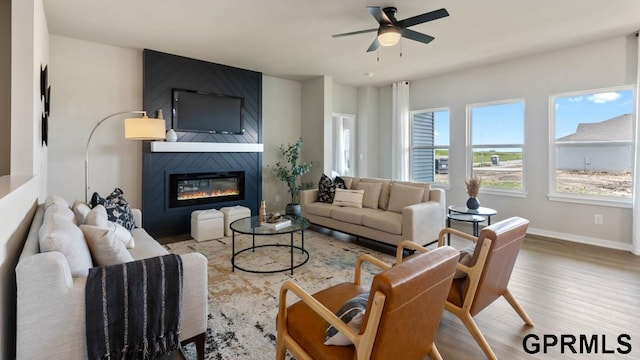 living room featuring ceiling fan, hardwood / wood-style flooring, and a large fireplace