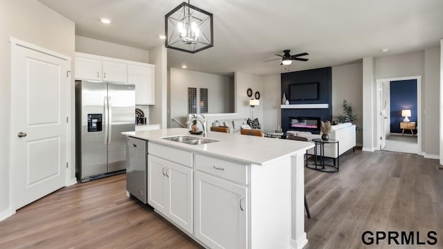 kitchen featuring appliances with stainless steel finishes, white cabinets, ceiling fan with notable chandelier, a kitchen island with sink, and sink