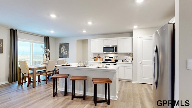 kitchen featuring white cabinets, a kitchen island with sink, stainless steel appliances, a breakfast bar area, and light hardwood / wood-style floors