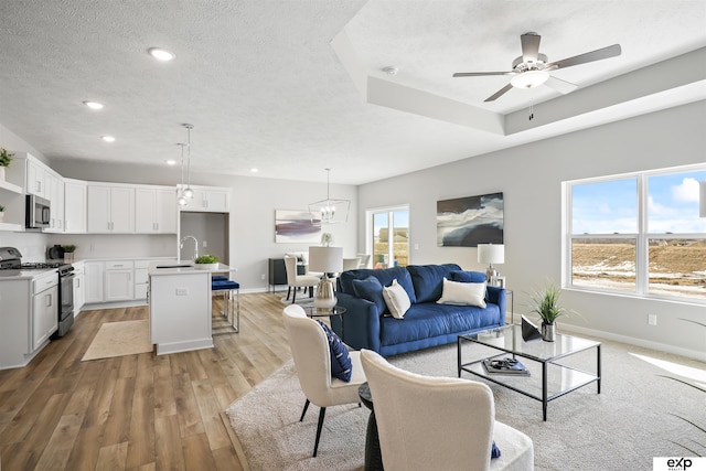 living room featuring a ceiling fan, a textured ceiling, baseboards, light wood-style floors, and recessed lighting