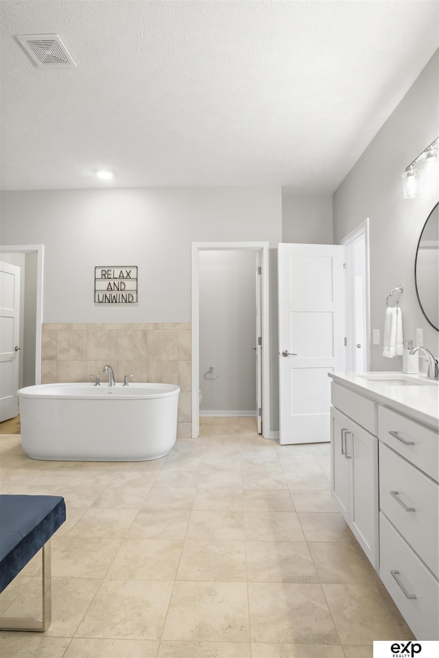full bath featuring visible vents, a textured ceiling, a freestanding bath, and vanity