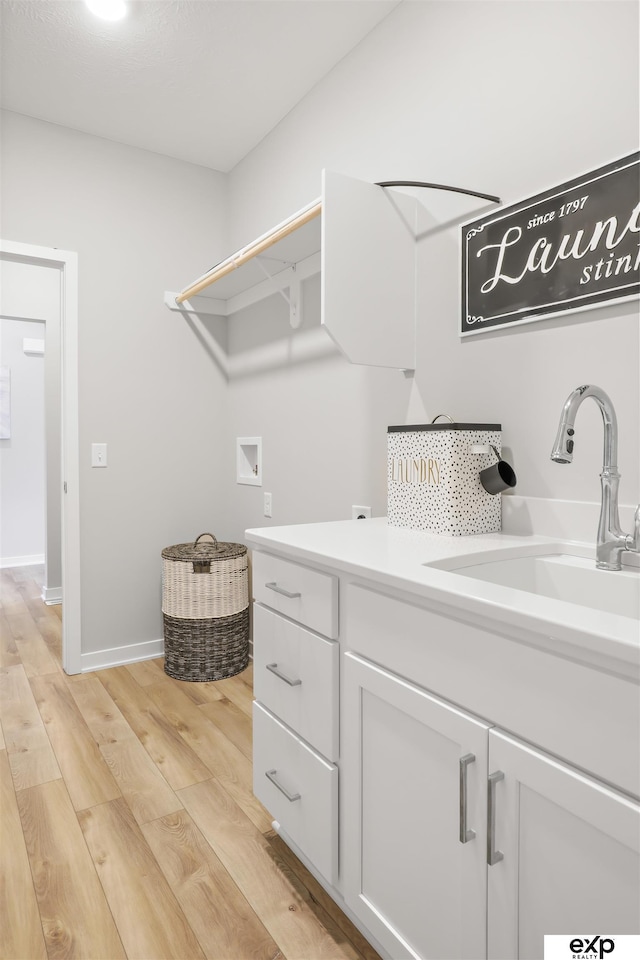 laundry room featuring cabinet space, a sink, hookup for a washing machine, light wood-style flooring, and baseboards