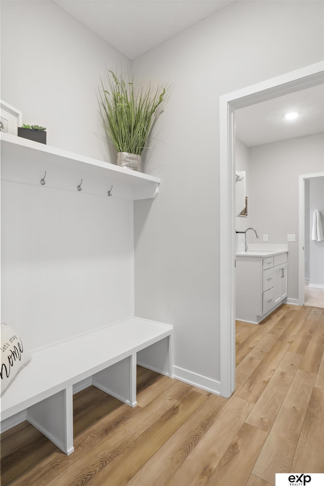 mudroom with light wood-style floors, a sink, and baseboards