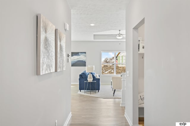 hallway featuring baseboards, a textured ceiling, and wood finished floors