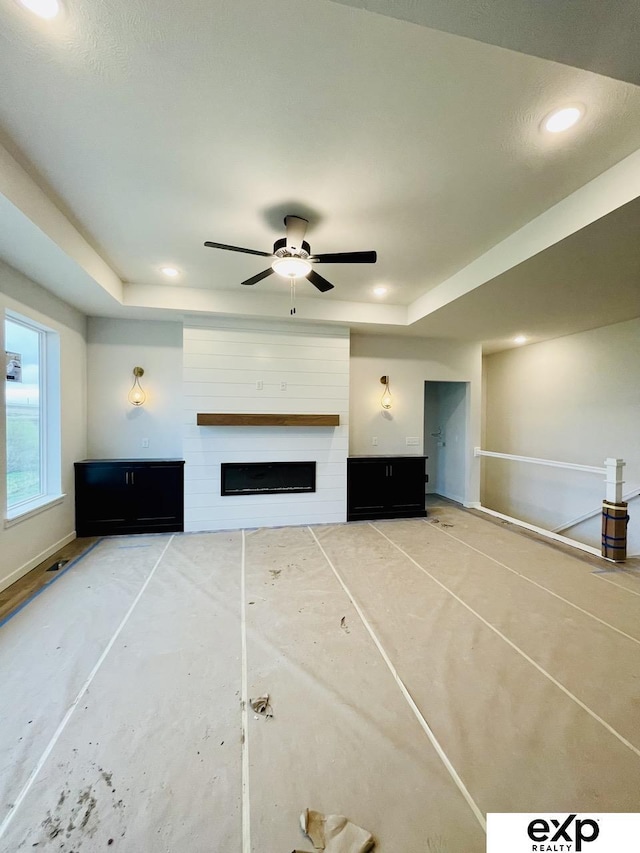 unfurnished living room with recessed lighting, ceiling fan, a large fireplace, and a raised ceiling