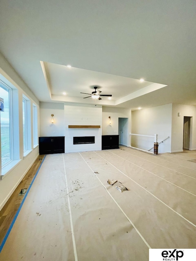 unfurnished living room with a ceiling fan, a raised ceiling, and a fireplace
