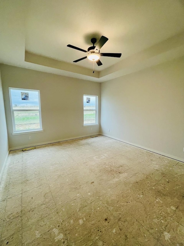 unfurnished room featuring a raised ceiling, baseboards, and ceiling fan