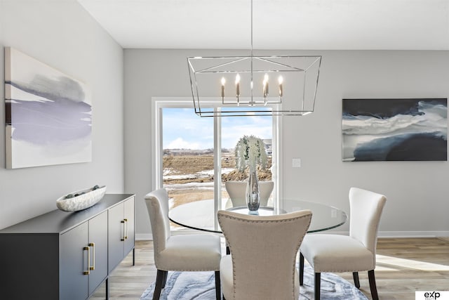 dining area featuring light wood-type flooring, baseboards, and a notable chandelier