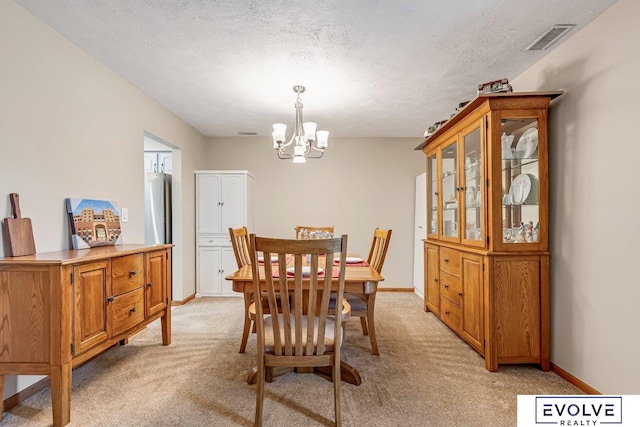 dining area with light carpet, a textured ceiling, and a chandelier