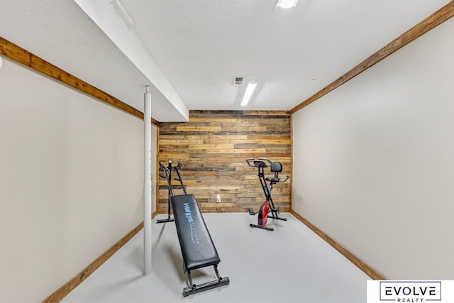 exercise area featuring a textured ceiling, wooden walls, and concrete floors