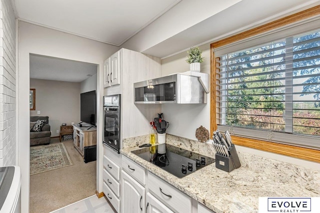 kitchen with light stone countertops, white cabinets, light colored carpet, and black electric cooktop