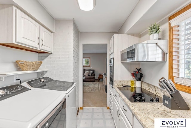 kitchen featuring black electric stovetop, light stone counters, white cabinetry, oven, and washing machine and dryer