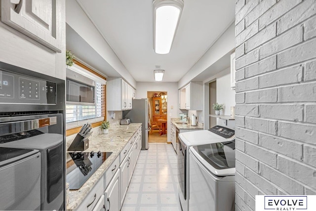 kitchen featuring washer and clothes dryer, stainless steel refrigerator, light stone countertops, and white cabinetry