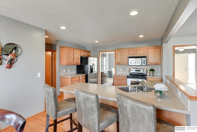 kitchen with light wood-type flooring, sink, a kitchen bar, stainless steel appliances, and backsplash