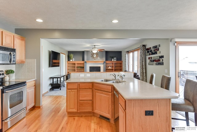 kitchen with sink, light hardwood / wood-style flooring, stainless steel appliances, a center island with sink, and ceiling fan