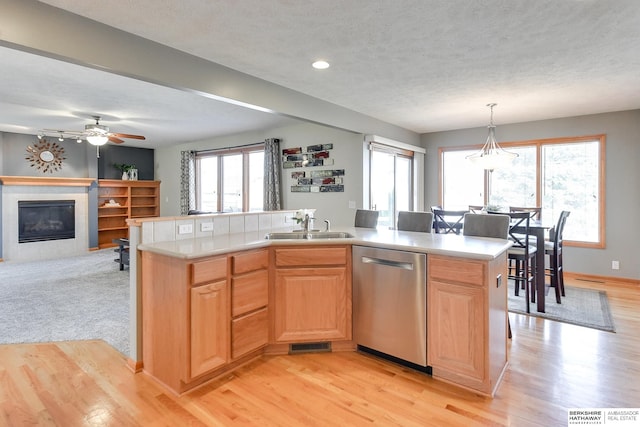 kitchen with ceiling fan, light wood-type flooring, stainless steel dishwasher, a center island with sink, and a fireplace