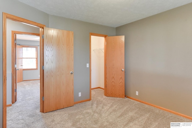 unfurnished bedroom with light colored carpet, a closet, a walk in closet, and a textured ceiling