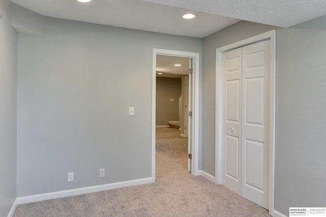 unfurnished bedroom featuring a textured ceiling, light colored carpet, and a closet