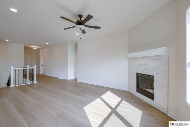 unfurnished living room with light hardwood / wood-style flooring, ceiling fan, and a stone fireplace