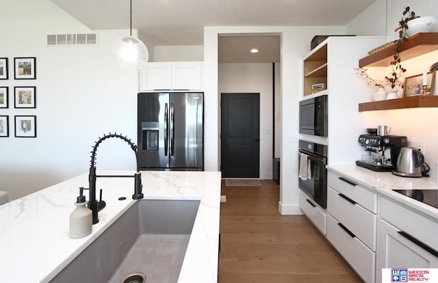 kitchen featuring hanging light fixtures, white cabinetry, light stone counters, black appliances, and sink