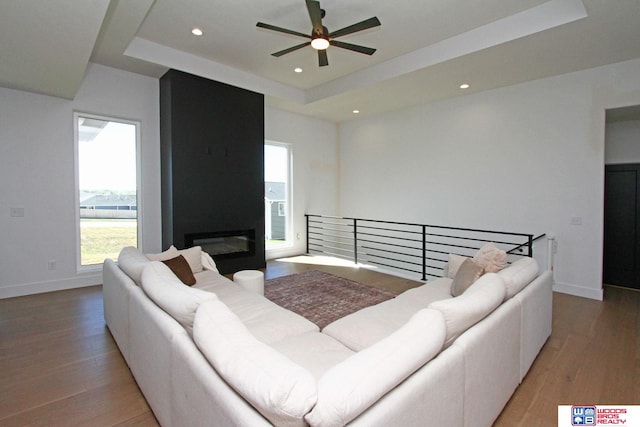 living room featuring ceiling fan, a fireplace, hardwood / wood-style floors, and a tray ceiling