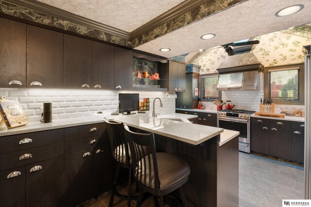 kitchen with a textured ceiling, stainless steel stove, kitchen peninsula, a kitchen breakfast bar, and ornamental molding