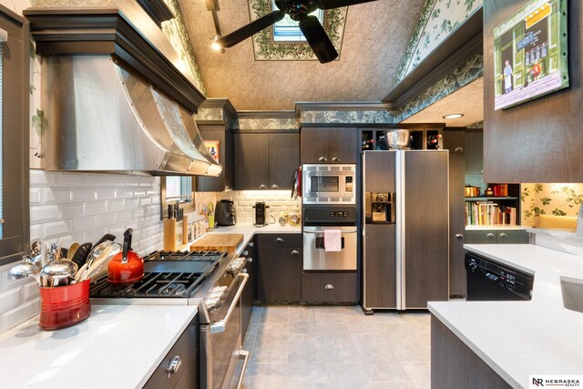 kitchen featuring dark brown cabinets, lofted ceiling, wall chimney range hood, stainless steel appliances, and ceiling fan