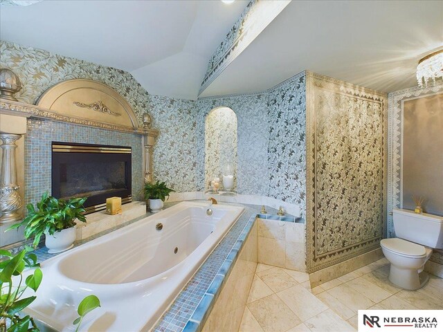 bathroom with toilet, lofted ceiling, tiled tub, a tiled fireplace, and tile patterned flooring