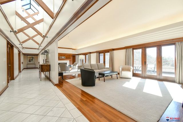 living room with high vaulted ceiling, light hardwood / wood-style floors, a skylight, and french doors