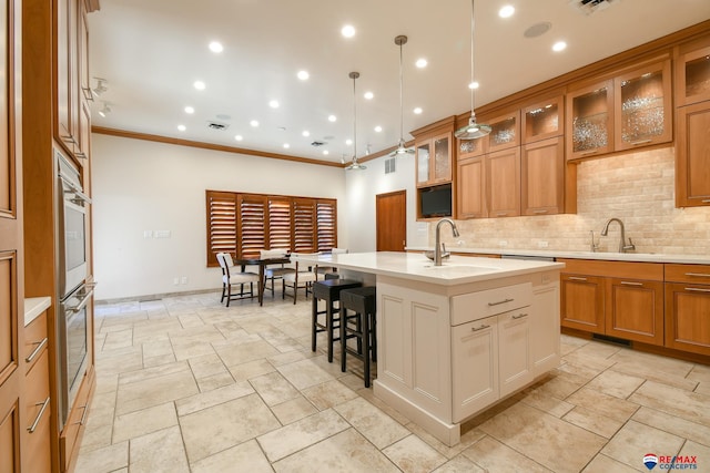 kitchen with a center island with sink, decorative backsplash, ornamental molding, and sink