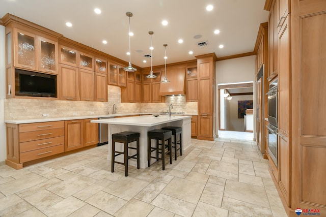 kitchen featuring hanging light fixtures, ornamental molding, tasteful backsplash, a kitchen island with sink, and a breakfast bar