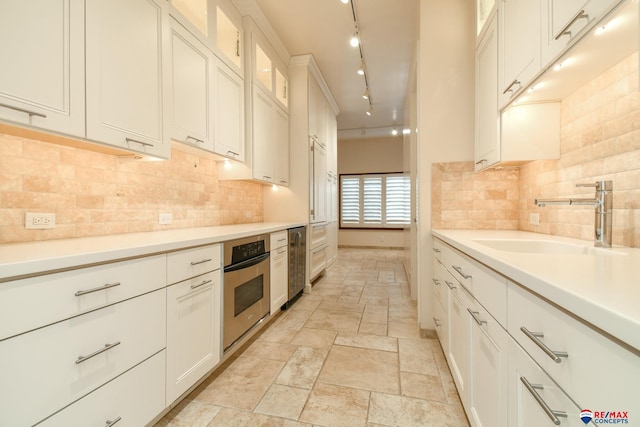 kitchen with rail lighting, white cabinetry, stainless steel oven, and sink