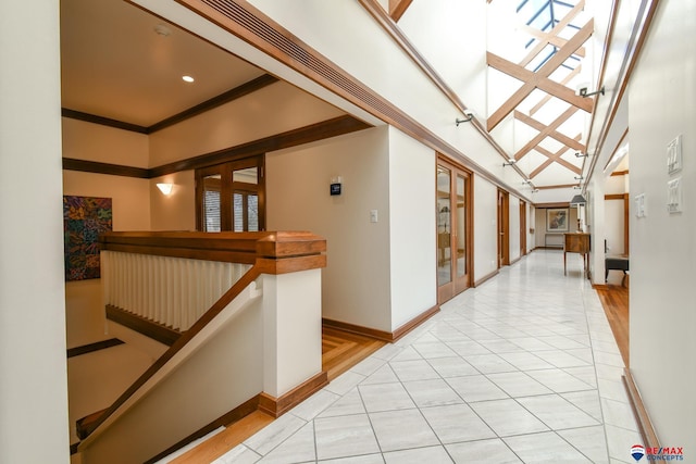 hall with light wood-type flooring, ornamental molding, and a towering ceiling