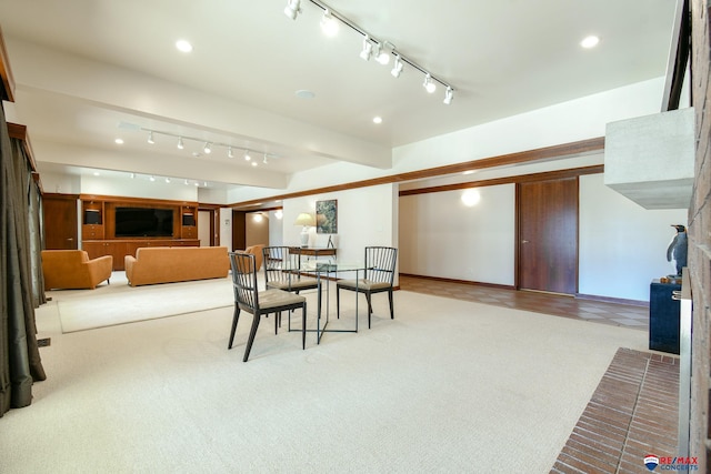 dining room featuring rail lighting, beamed ceiling, and light colored carpet