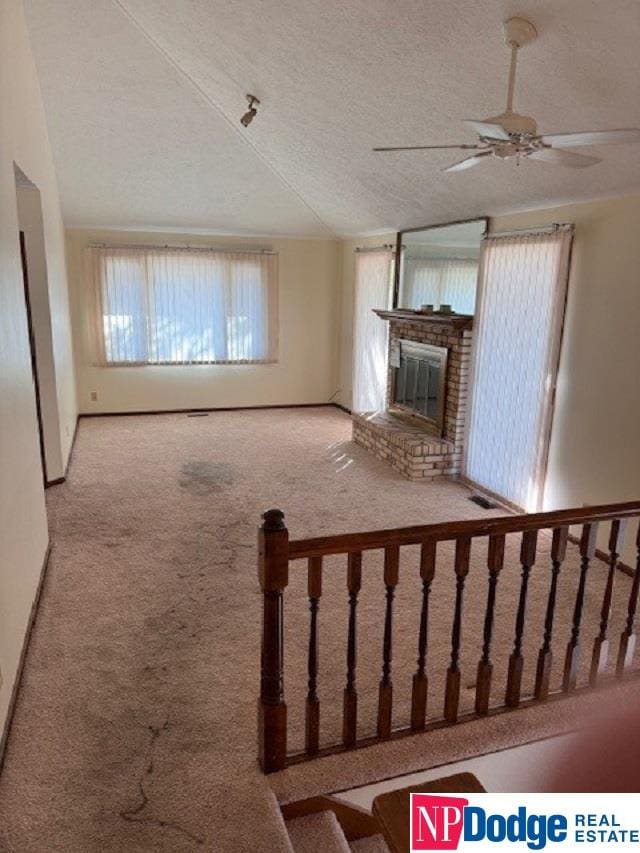 unfurnished living room featuring a brick fireplace, carpet, ceiling fan, vaulted ceiling, and a textured ceiling