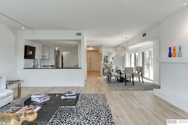 living room with light wood-type flooring, an inviting chandelier, and track lighting