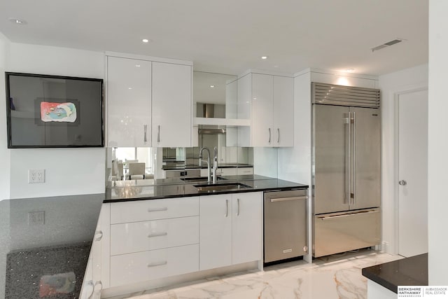 kitchen with dark stone counters, stainless steel built in fridge, white cabinetry, and sink