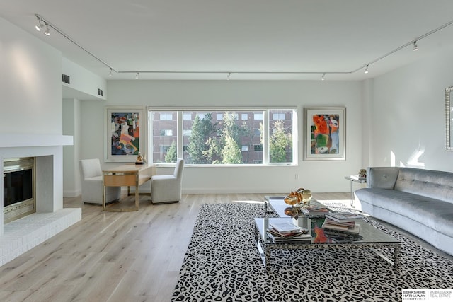 living room featuring a brick fireplace, light hardwood / wood-style flooring, and track lighting