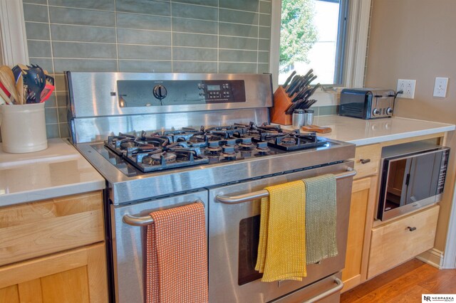 kitchen with appliances with stainless steel finishes, light hardwood / wood-style floors, light brown cabinetry, and tasteful backsplash