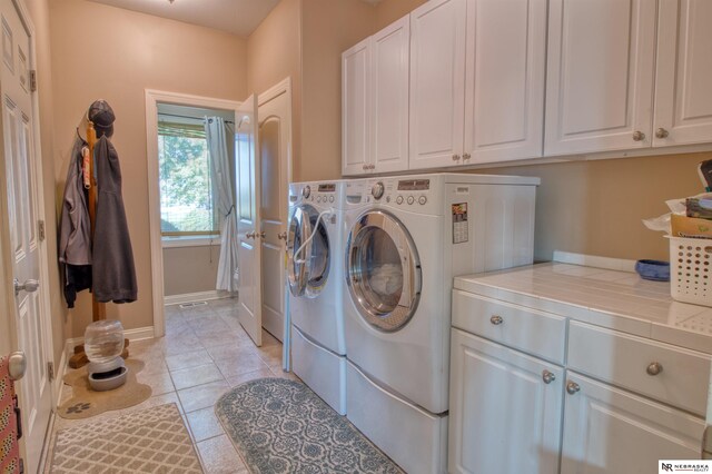 laundry area featuring separate washer and dryer, light tile patterned floors, and cabinets