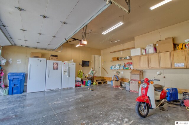 garage with a garage door opener, white fridge with ice dispenser, and white refrigerator