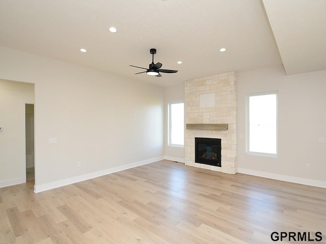 unfurnished living room with light hardwood / wood-style floors, a healthy amount of sunlight, and a stone fireplace