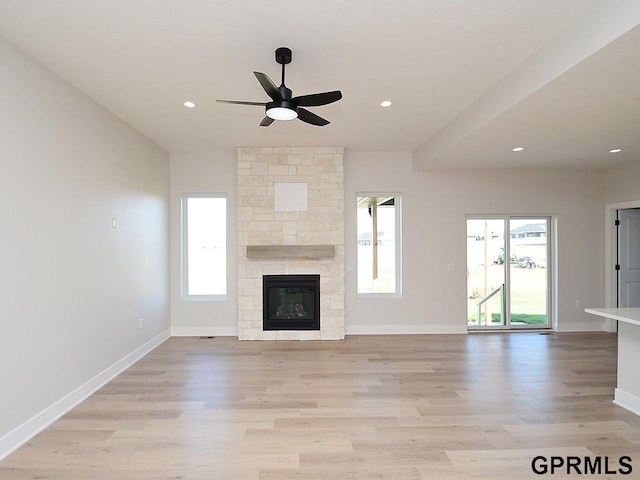 unfurnished living room featuring a stone fireplace, light hardwood / wood-style floors, and ceiling fan