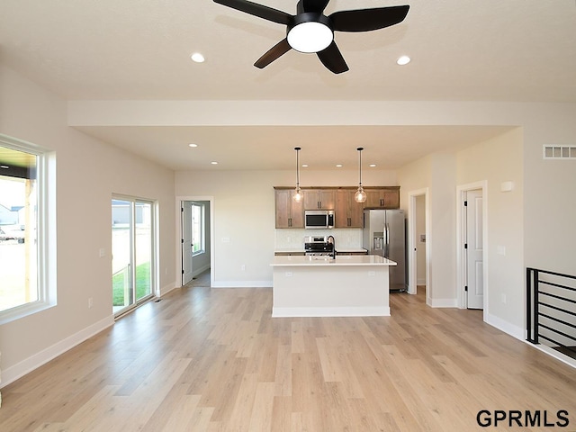 kitchen with pendant lighting, stainless steel appliances, light hardwood / wood-style flooring, a kitchen island with sink, and sink