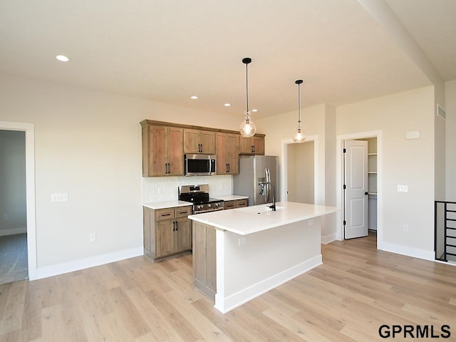 kitchen with decorative light fixtures, a center island with sink, stainless steel appliances, and light hardwood / wood-style flooring