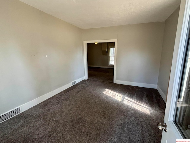 spare room with a textured ceiling and dark colored carpet