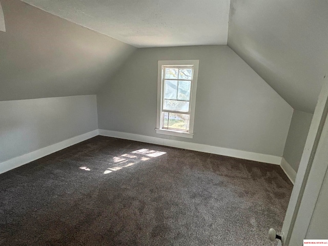 additional living space featuring vaulted ceiling and dark colored carpet